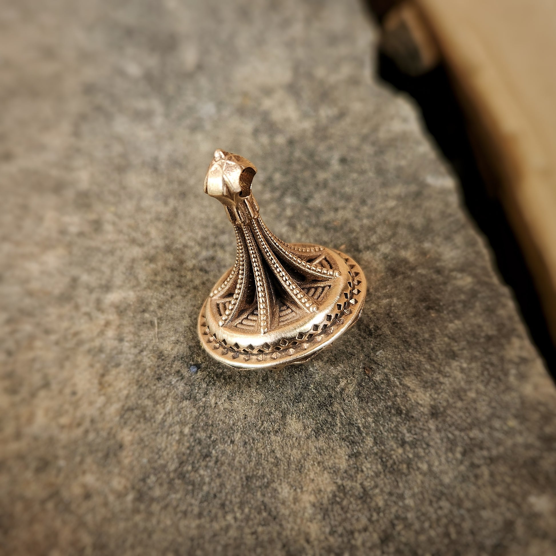 Antiqued bronze spinning top that functions as a pendant.