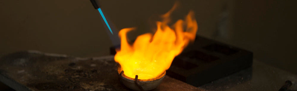 Flame from a jewelry torch heating up a crucible on a workbench